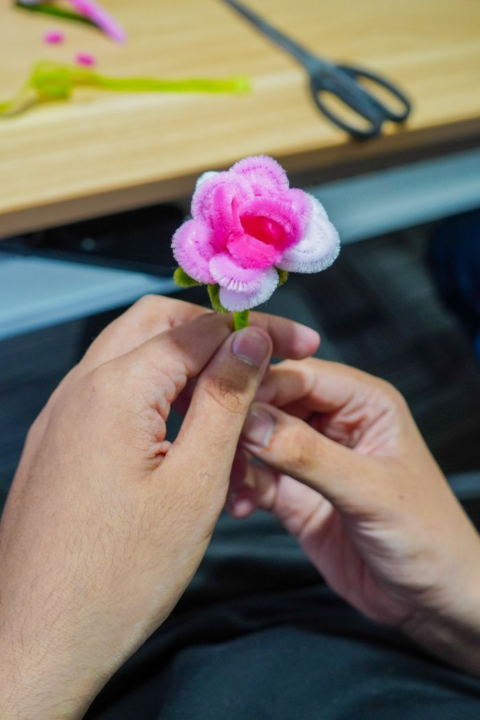 Close-up of hands crafting a pink pipe cleaner flower on a table.