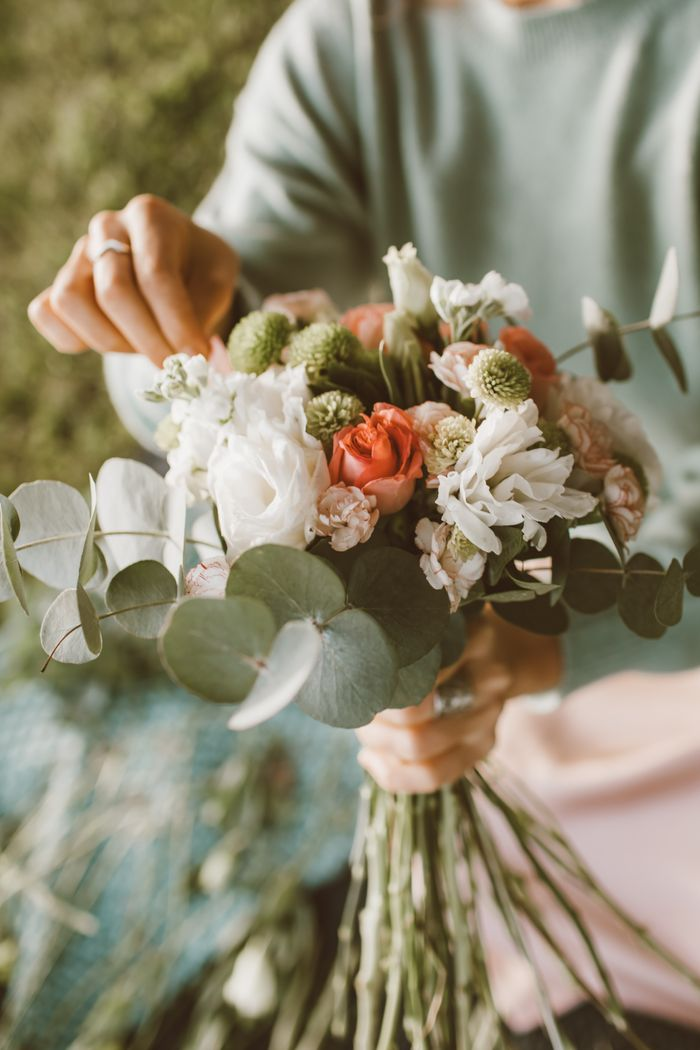 Offerings A close-up of hands arranging a beautiful bouquet with roses and greenery.